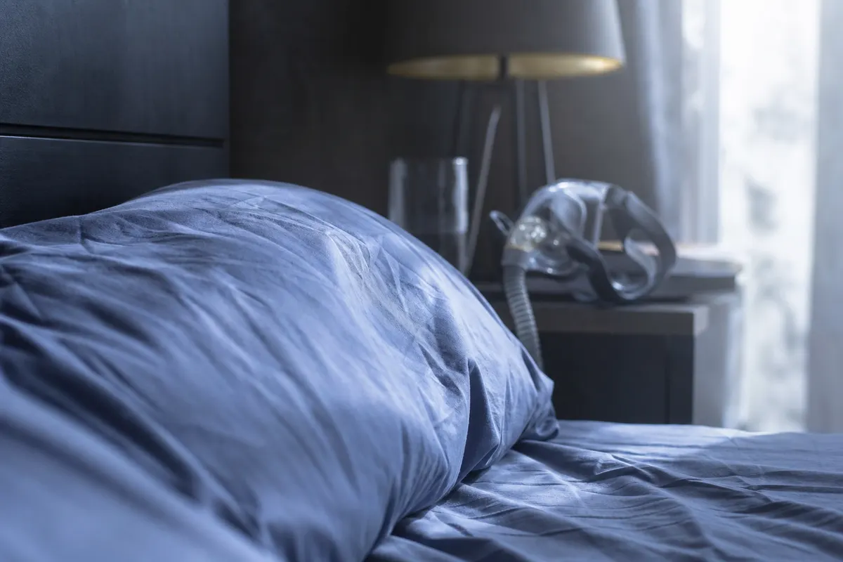 Chambre calme au petit matin, lumière naturelle douce sur un oreiller et un masque respiratoire posé de côté, aucun visage ni texte visible.