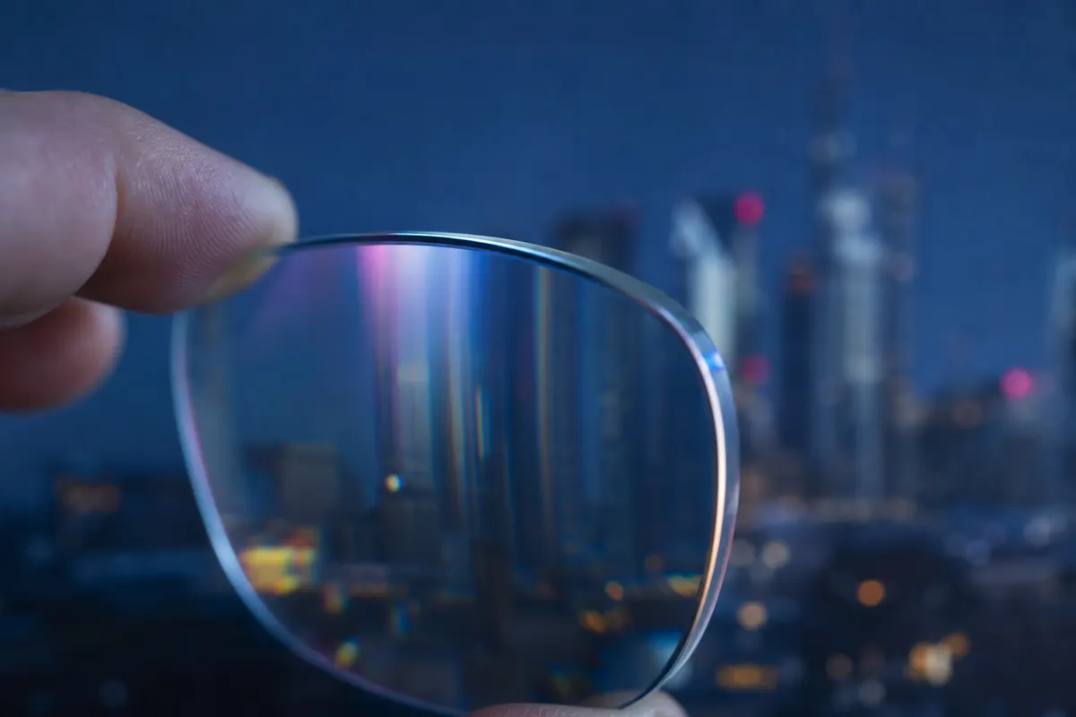 Gros plan sur un verre de lunettes correcteur légèrement incliné, laissant apparaître une déformation optique caractéristique en arrière-plan flou.