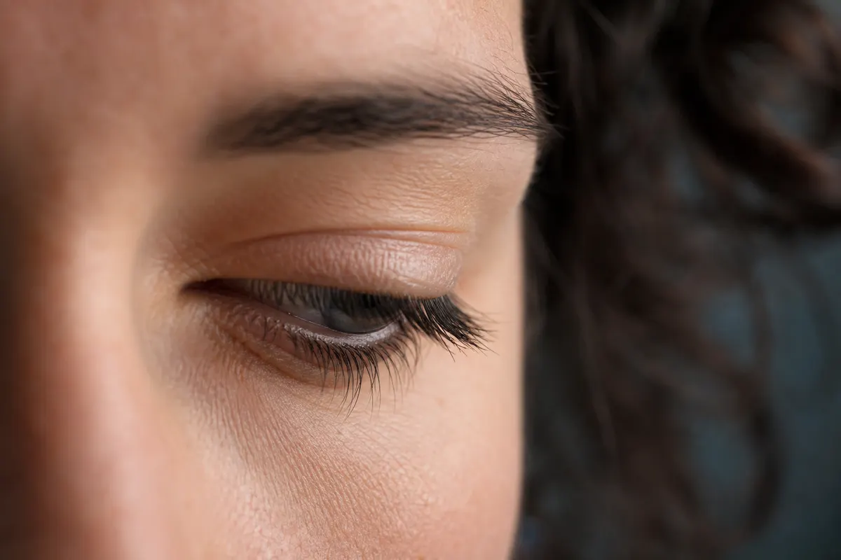 Gros plan calme sur le contour d'un œil légèrement fermé, lumière naturelle douce, aucun autre détail du visage visible.