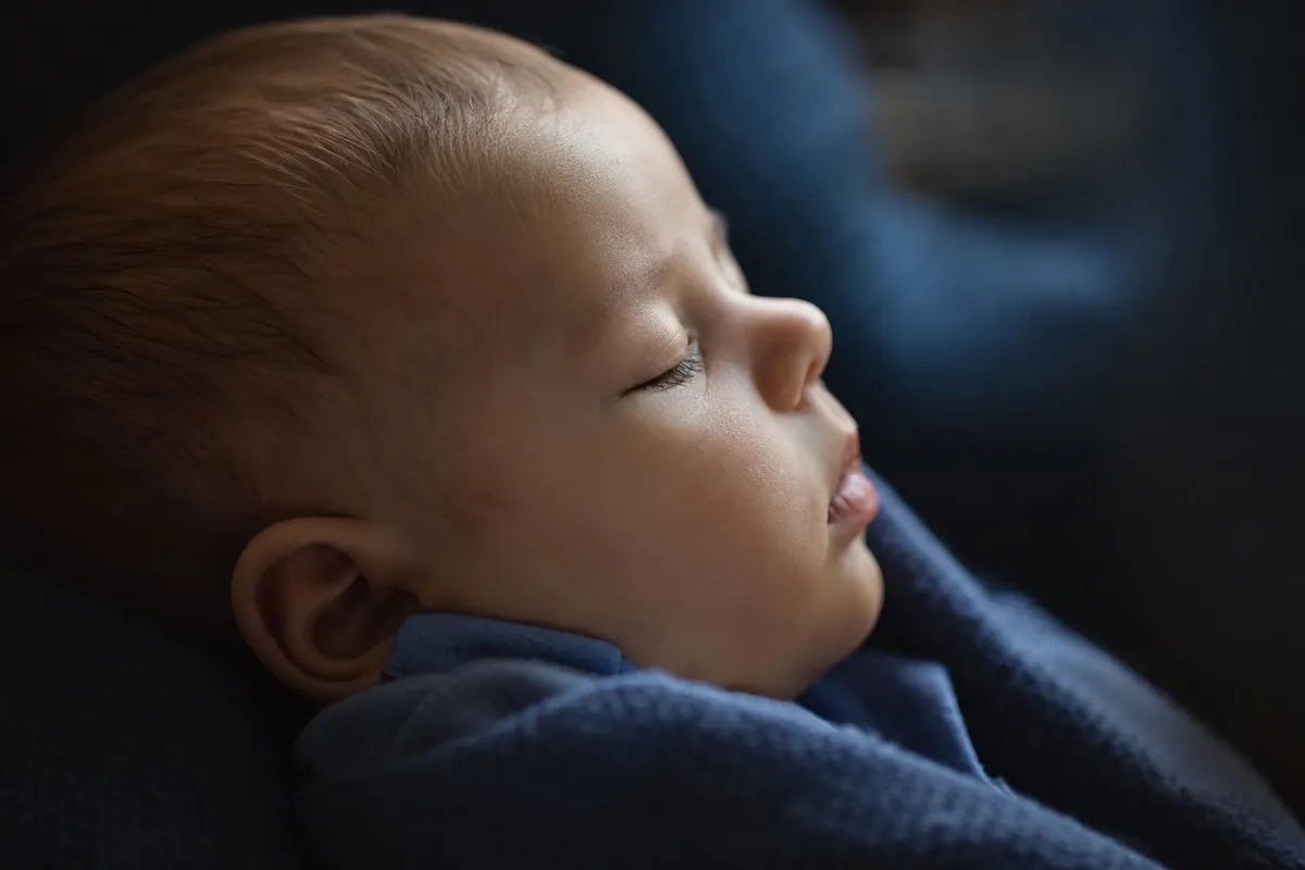 Visage de bébé de profil discret, lumière naturelle douce, aucune sécrétion ni texte visible dans le cadre.