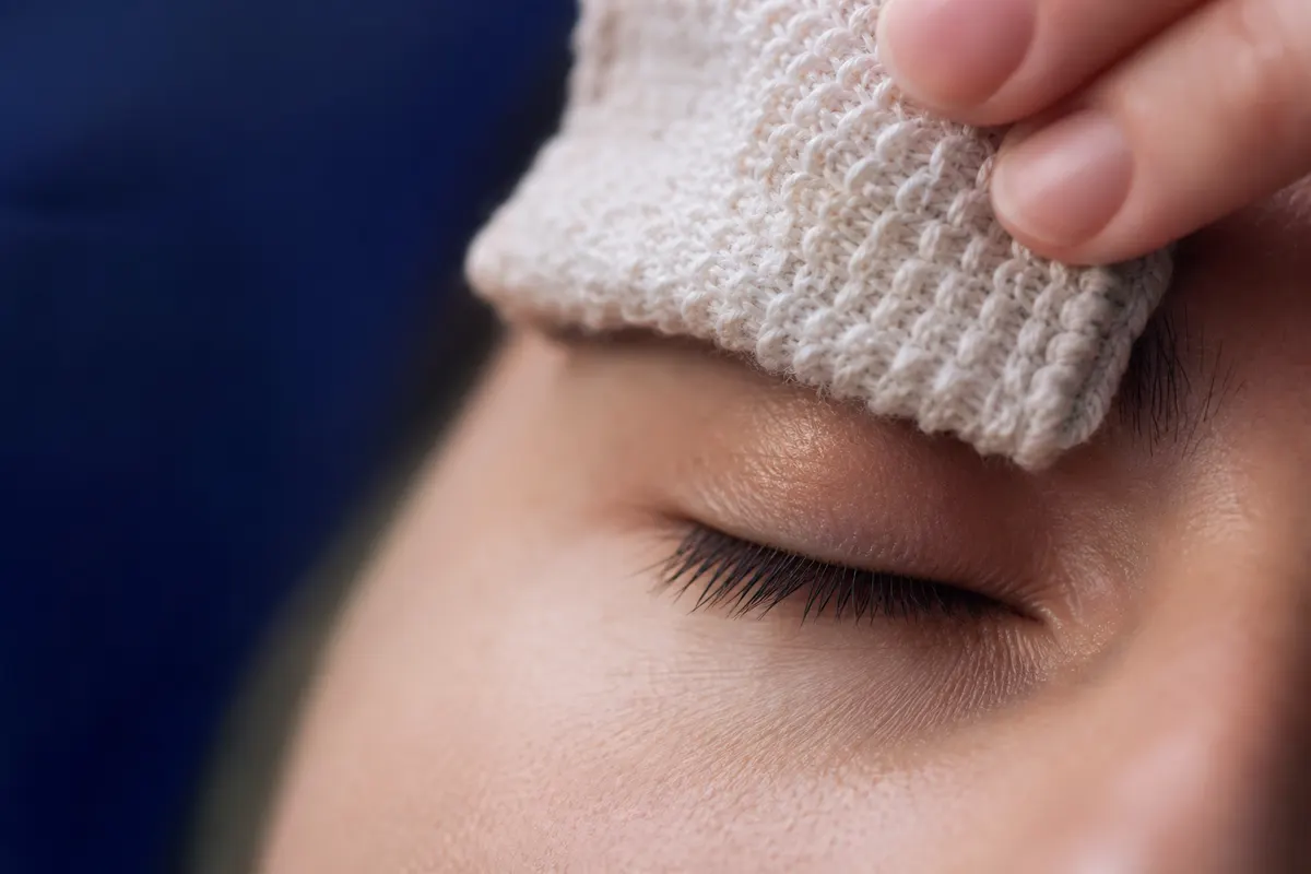 Gros plan calme sur le contour d'une paupière, geste doux d'application d'une compresse tiède, lumière naturelle douce, aucun visage entièrement visible.