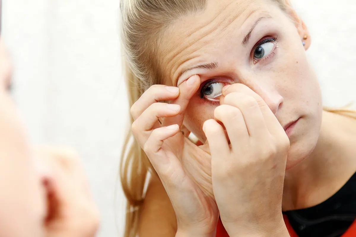Personne se lavant et séchant ses mains avant de manipuler une lentille de contact devant un miroir.