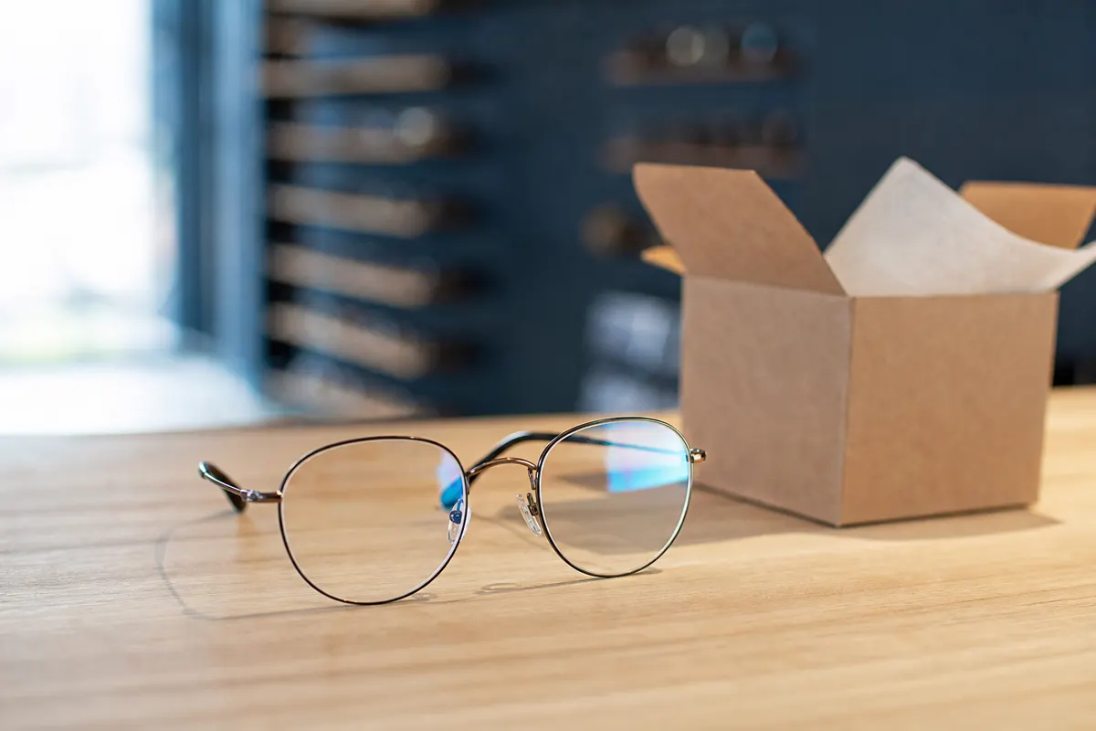 Une paire de lunettes de vue posée sur un comptoir d'opticien, à côté d'un colis en carton ouvert, lumière naturelle douce.