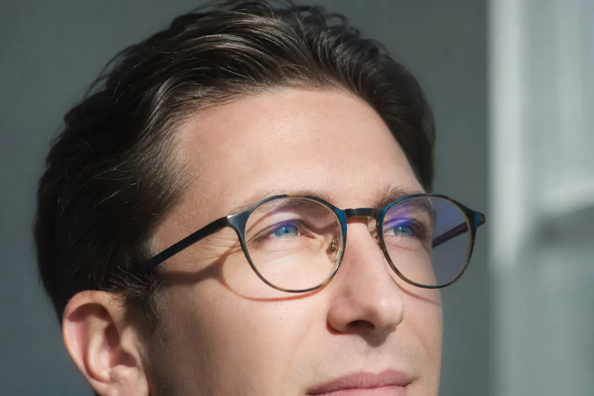 Gros plan calme sur une personne plissant légèrement les yeux face à une lumière douce filtrant par une fenêtre, aucun autre détail visible.