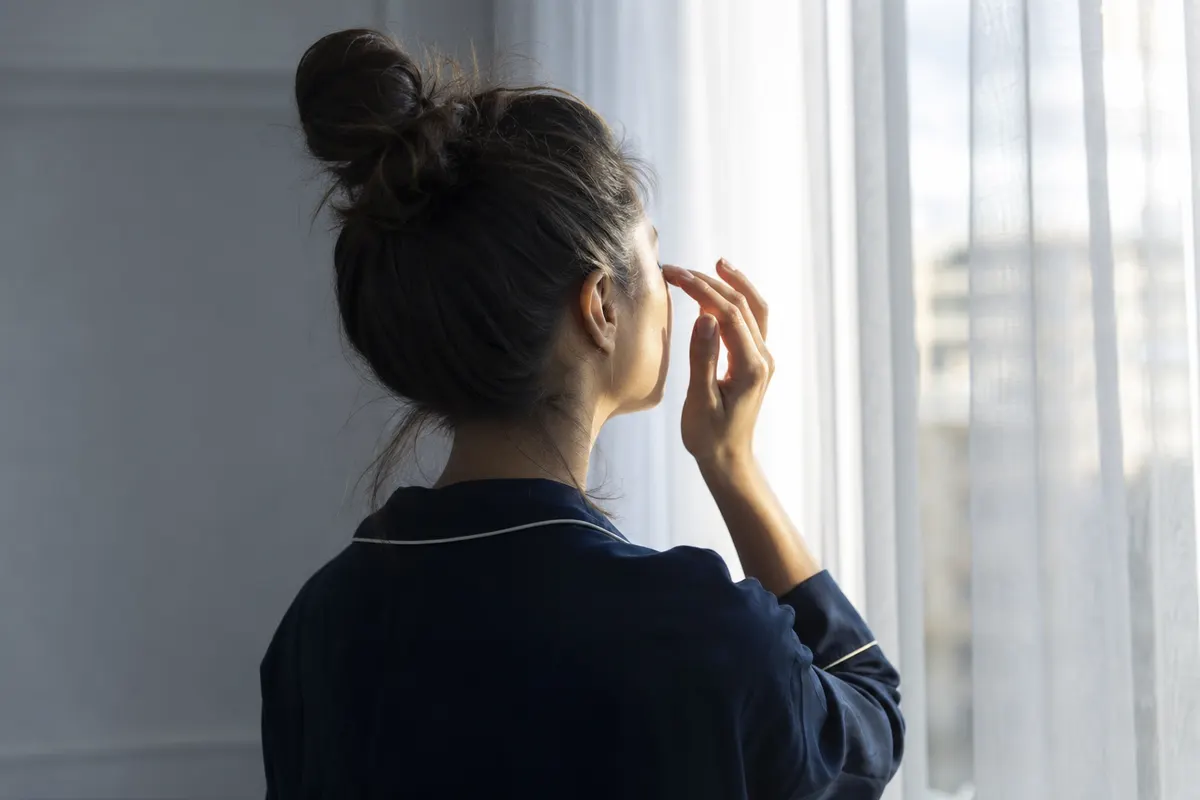 Femme clignant doucement des yeux devant une fenêtre lumineuse, lumière naturelle douce, aucun autre détail visible.