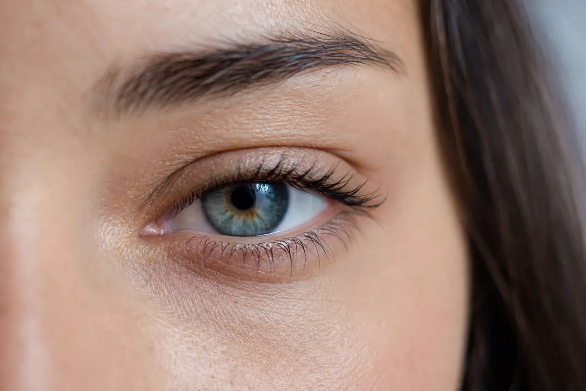 Gros plan calme sur le contour d'un œil avec une paupière légèrement abaissée, lumière naturelle douce, aucun autre détail du visage visible.