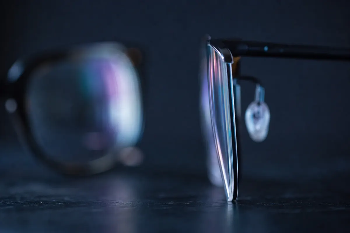 Profil d'une paire de lunettes à verres fins posée sur une table sombre, tranche du verre visible et nettement plus fine que sur une monture classique en arrière-plan flou.