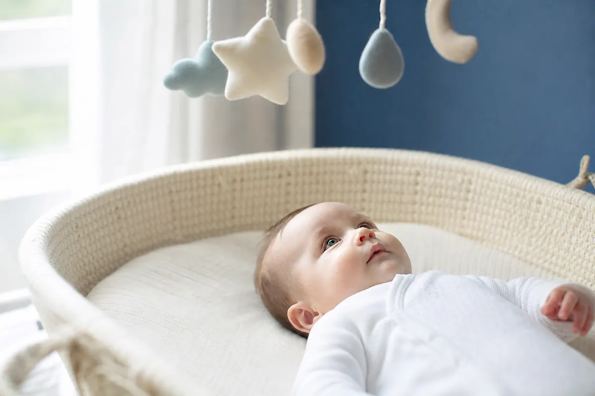 Bébé allongé sur le dos qui regarde un mobile suspendu au-dessus de lui, dans une chambre baignée de lumière naturelle douce.